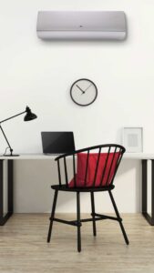 Minimal home office desk with a laptop, black desk lamp, red-cushioned chair, wall clock, and wall-mounted AC on a white wall.