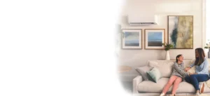 Mother and daughter sit on a beige sofa in a bright living room, smiling and holding hands as they chat.